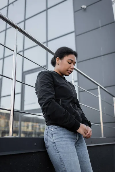 Niedriger Blickwinkel auf eine depressive Frau, die in der Nähe eines verschwommenen Gebäudes im Freien steht — Stockfoto