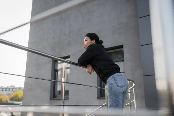 Seitenansicht einer traurigen multirassischen Frau mit Apathie, die am Geländer der städtischen Straße steht — Stockfoto