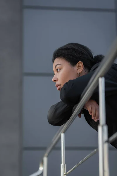 Jeune femme multiraciale avec apathie regardant loin près de rambarde à l'extérieur — Photo de stock