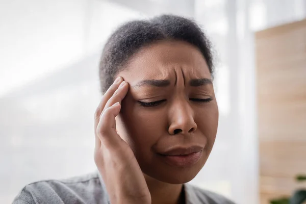 Jeune femme multiraciale souffrant de douleur à la tête à la maison — Photo de stock