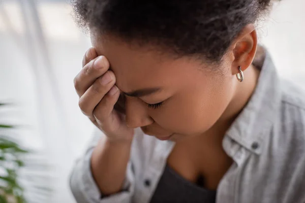 Disappointed multiracial woman with anxiety touching head at home — Stock Photo