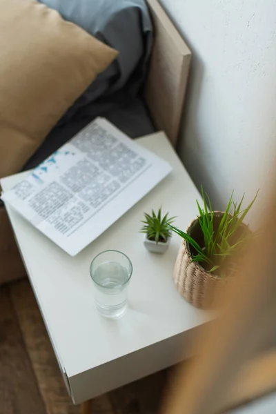 High angle view of glass of water and newspaper on bedside table in bedroom — Stock Photo
