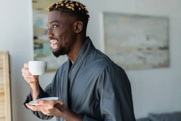 Smiling african american man with vitiligo holding cup of coffee at home — Stock Photo