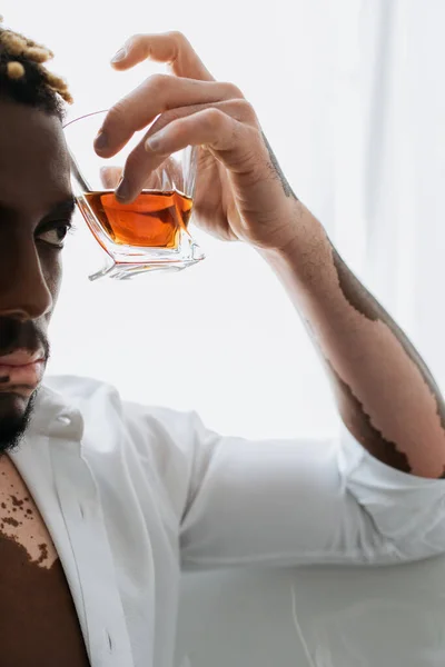 Vista ritagliata dell'uomo afro-americano con vitiligine in possesso di whisky mentre seduto nella vasca da bagno — Foto stock