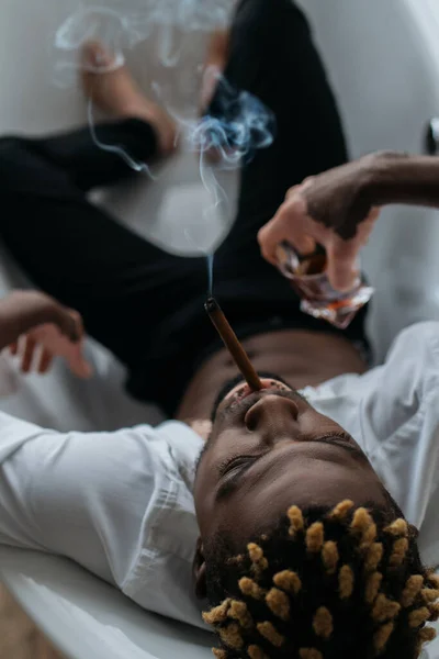 Vista aérea del hombre afroamericano con vitiligo fumando cigarro y sosteniendo whisky en la bañera - foto de stock