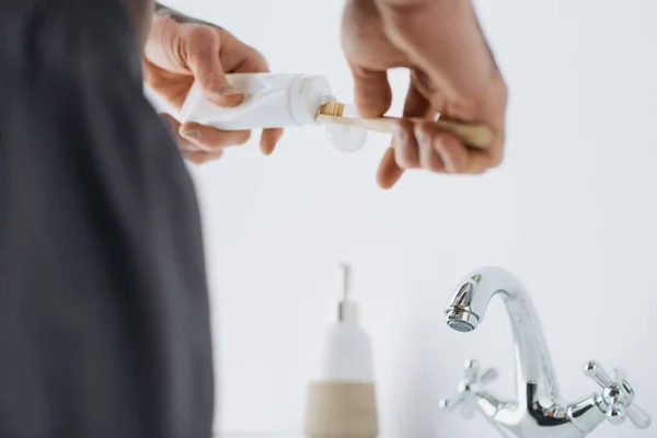 Vista recortada del hombre afroamericano con vitiligo apretando la pasta de dientes en el cepillo de dientes cerca del lavabo en el baño - foto de stock