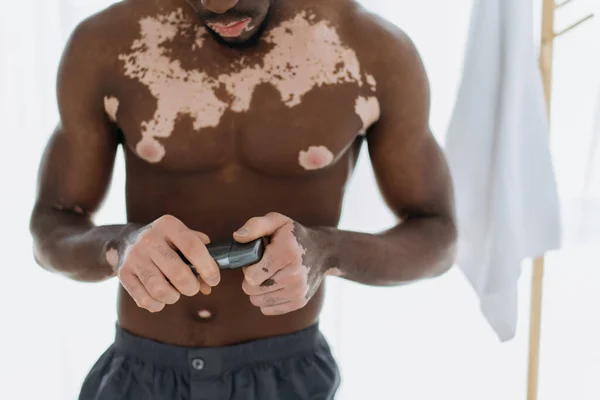 Vista recortada del hombre afroamericano sin camisa con vitiligo sosteniendo desodorante en el baño - foto de stock