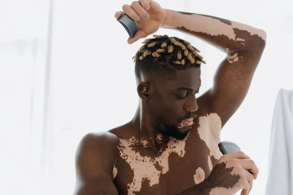 Африканский мужчина без рубашки с витилиго с дезодорантом в ванной комнате — стоковое фото