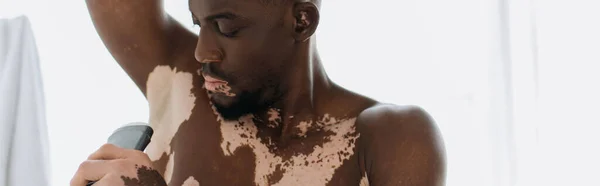 African american man with vitiligo holding deodorant in bathroom, banner — Stock Photo