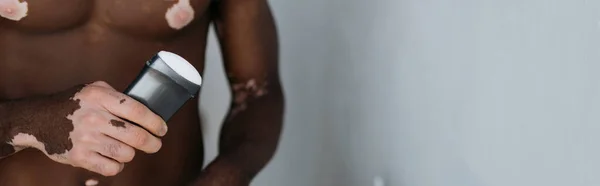 Cropped view of muscular african american man with vitiligo holding deodorant at home, banner — Stock Photo