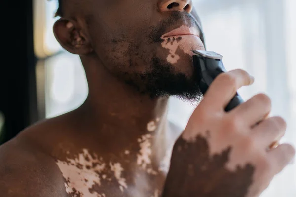 Vista cortada do homem americano africano com vitiligo barbear com navalha elétrica de manhã — Fotografia de Stock