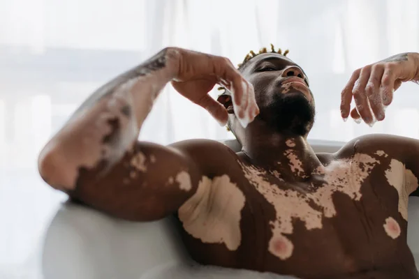 Hombre afroamericano con vitiligo tomando baño en casa - foto de stock