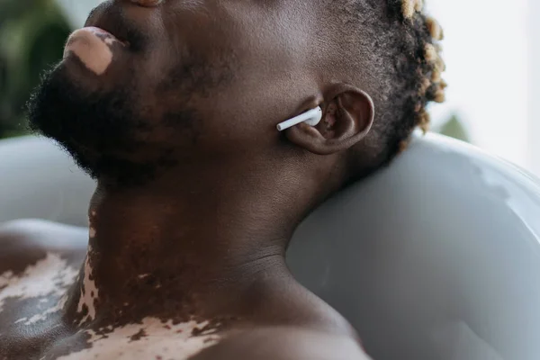 Vue recadrée de l'homme afro-américain avec vitiligo en utilisant un écouteur tout en prenant un bain à la maison — Photo de stock