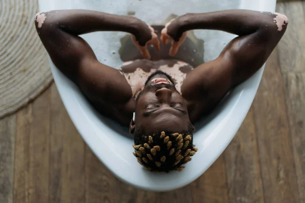 Visão aérea do homem afro-americano com vitiligo ouvir música e tomar banho em casa — Fotografia de Stock