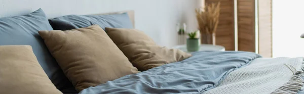 Oreillers et couvertures sur lit dans une chambre floue, bannière — Photo de stock
