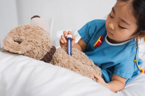 Bambina asiatica che fa l'iniezione a orsacchiotto con siringa giocattolo mentre gioca in ospedale — Foto stock
