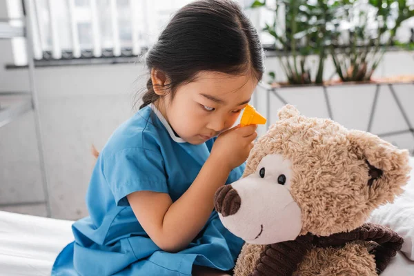 Pouco ásia menina jogar no clínica e examinar ursinho de pelúcia com brinquedo otoscópio — Fotografia de Stock