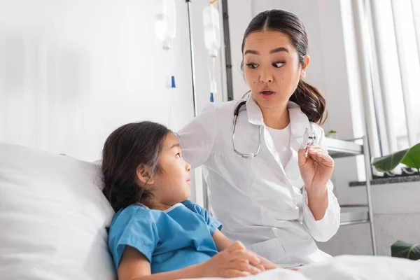 Asiatischer Arzt zeigt Stethoskop und spricht mit kleinem Patienten in Kinderklinik — Stockfoto