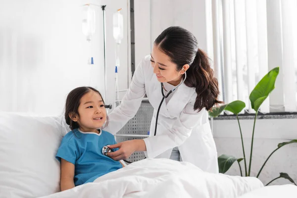 Jeune asiatique médecin avec stéthoscope examen joyeuse fille dans pédiatrie hôpital — Photo de stock