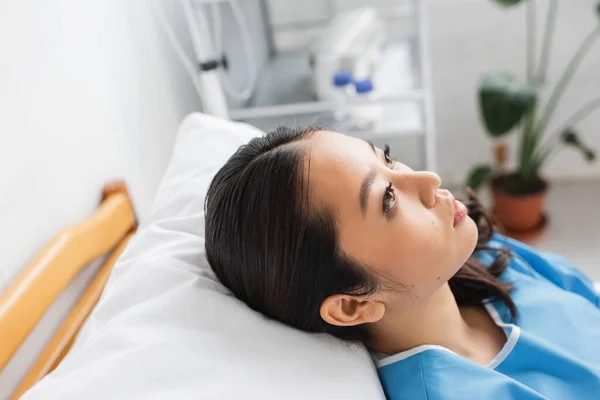 Пригнічена азіатська жінка лежить на ліжку в лікарняному палаті і дивиться геть — стокове фото