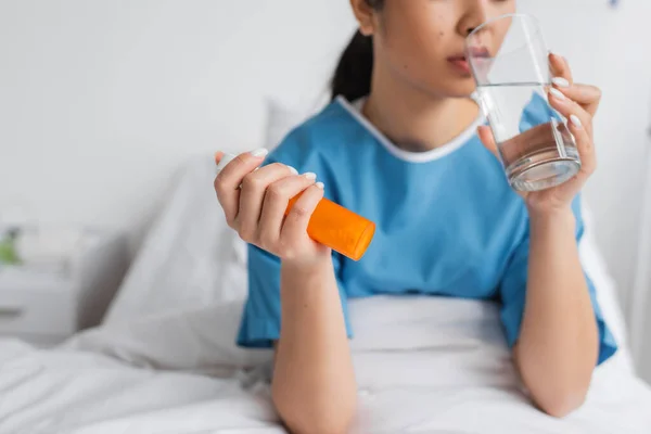 Частичный взгляд на больную женщину с контейнером для таблеток и питьевой водой в больничном отделении — стоковое фото