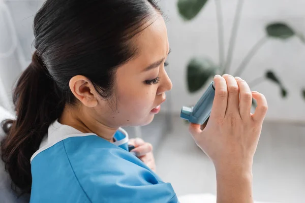 Side view of diseased asian woman holding inhaler in hospital ward — Stock Photo