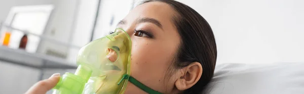 Хвора азіатська жінка, дивлячись далеко під час дихання в кисневій масці в лікарні, банер — стокове фото