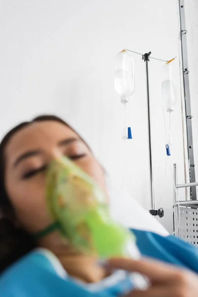 Desfocado ásia mulher com fechado olhos respirando no oxigênio máscara no hospital ward — Fotografia de Stock