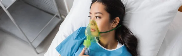 Top view de deprimido asiático mulher em oxigênio máscara olhando para longe na cama no hospital ward, banner — Fotografia de Stock