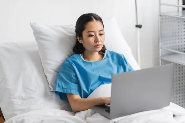 Junge Asiatin arbeitet auf Laptop im Bett auf Krankenhausstation — Stockfoto