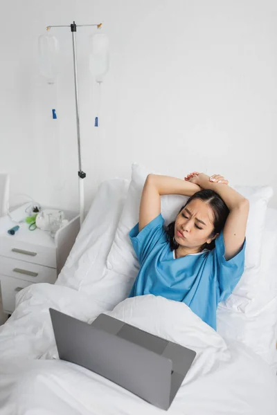 Disgustado asiático mujer mirando portátil mientras viendo película en hospital sala - foto de stock