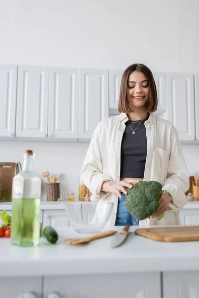 Радостная женщина, держащая брокколи рядом с разделочной доской на кухне — стоковое фото