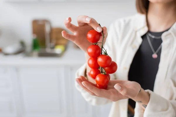 Cropped view of blurred woman holding cherry tomatoes in kitchen — Stock Photo