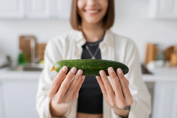 Cropped view of blurred woman holding ripe cucumber in kitchen — Stock Photo