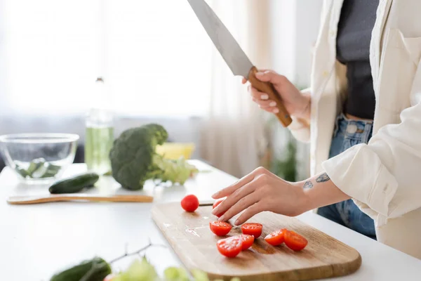 Vista cortada de mulher tatuada segurando faca perto de tomates cereja na cozinha — Fotografia de Stock