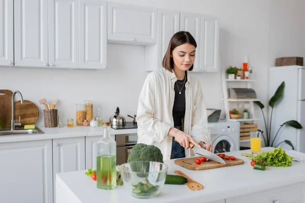 Жінка з Брюнета ріже вишневі помідори біля органічних овочів на кухні. — стокове фото