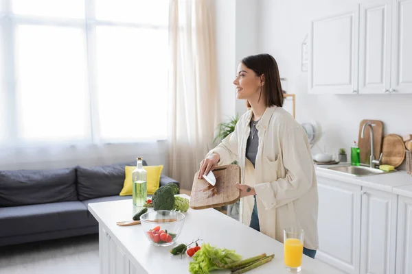 Seitenansicht einer lächelnden Frau, die in der Küche frischen Salat kocht — Stockfoto