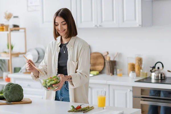 Mujer sonriente sosteniendo tazón con ensalada fresca en la cocina en casa - foto de stock