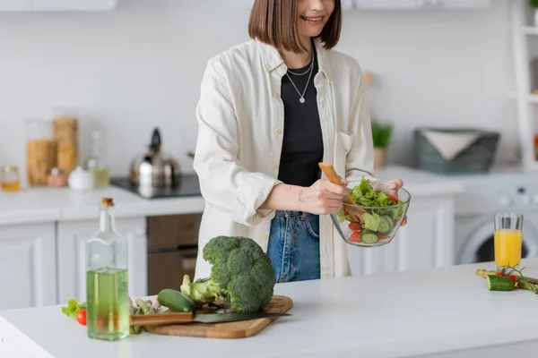 Обрезанный вид веселой женщины, держащей миску со свежим салатом на кухне — стоковое фото