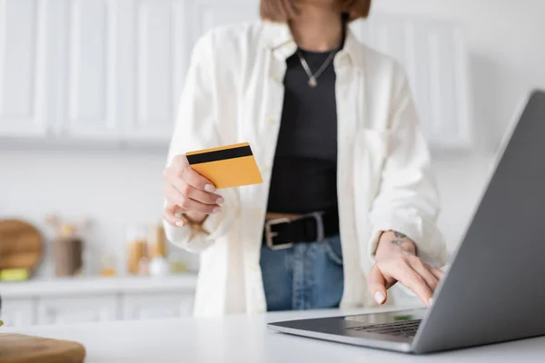 Vista recortada de la mujer borrosa que sostiene la tarjeta de crédito mientras pide comida en el ordenador portátil en casa - foto de stock