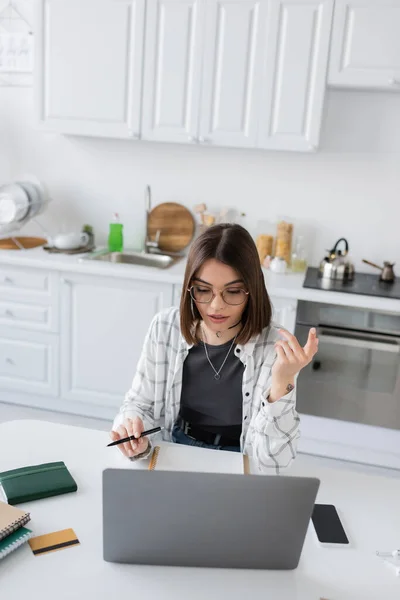 Freelancer in eyeglasses using laptop near notebooks and credit card in kitchen — Stock Photo