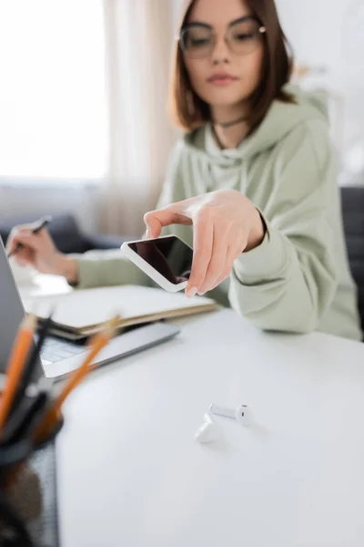 Freelance floue prenant smartphone près des écouteurs sur la table à la maison — Photo de stock