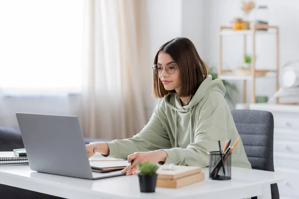 Brunette freelancer using laptop near notebooks and books at home — Stock Photo