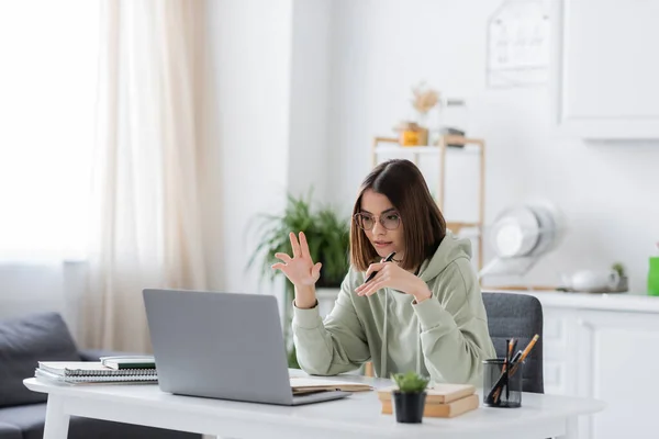 Freelancer em óculos ter chat de vídeo no laptop perto de notebooks em casa — Fotografia de Stock