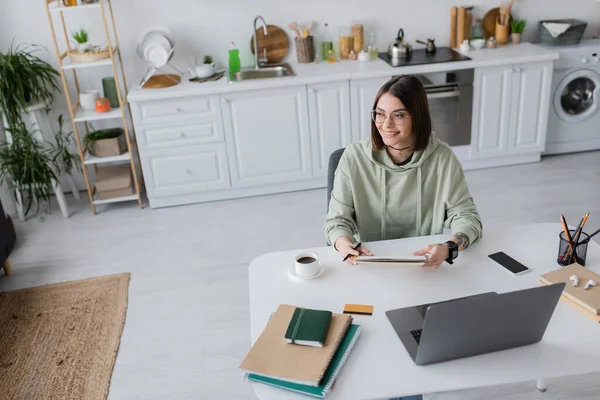 Overjoyed freelancer holding notebook near gadgets and coffee at home — Stock Photo