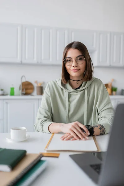 Young freelancer looking at camera near blurred laptop and coffee at home — Stock Photo