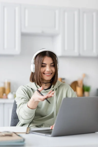 Positive freelancer in headphones having video call on blurred laptop at home — Stock Photo