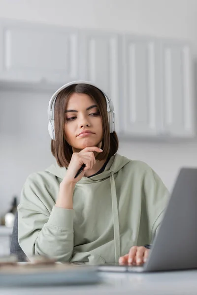 Pensive freelancer in headphones using blurred laptop at home — Stock Photo
