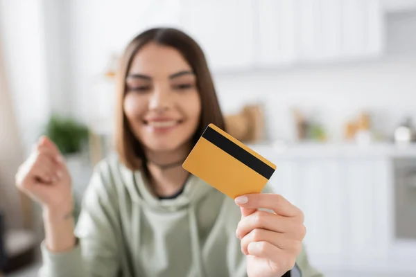 Young blurred woman holding credit card and smiling at home — Stock Photo