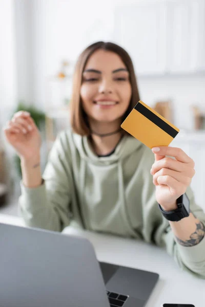 Весела брюнетка, що тримає кредитну картку біля ноутбука під час онлайн-покупки вдома — стокове фото